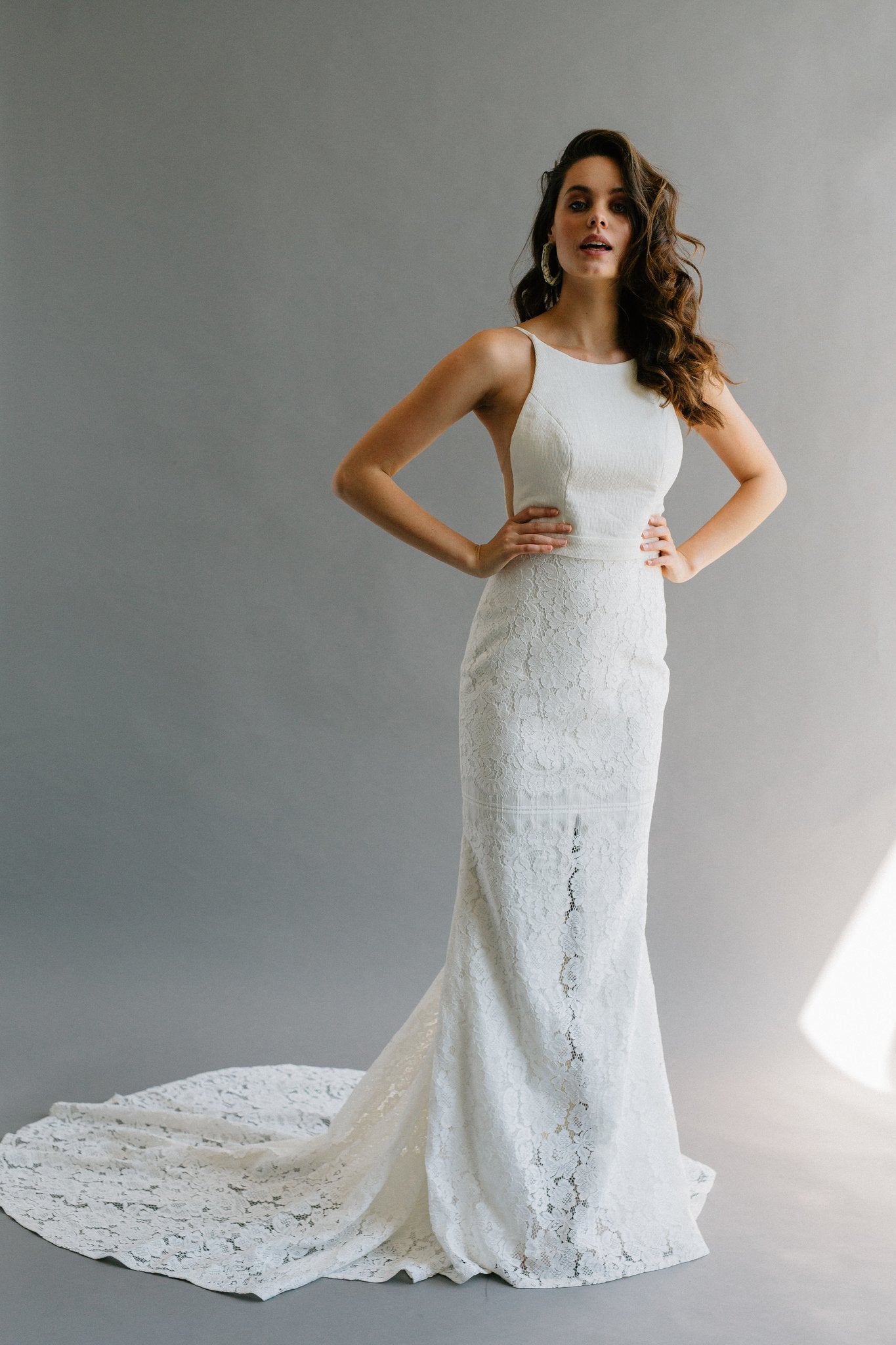 A modern fitted wedding dress with a high neck, low back, and hidden slit in the lace skirt.